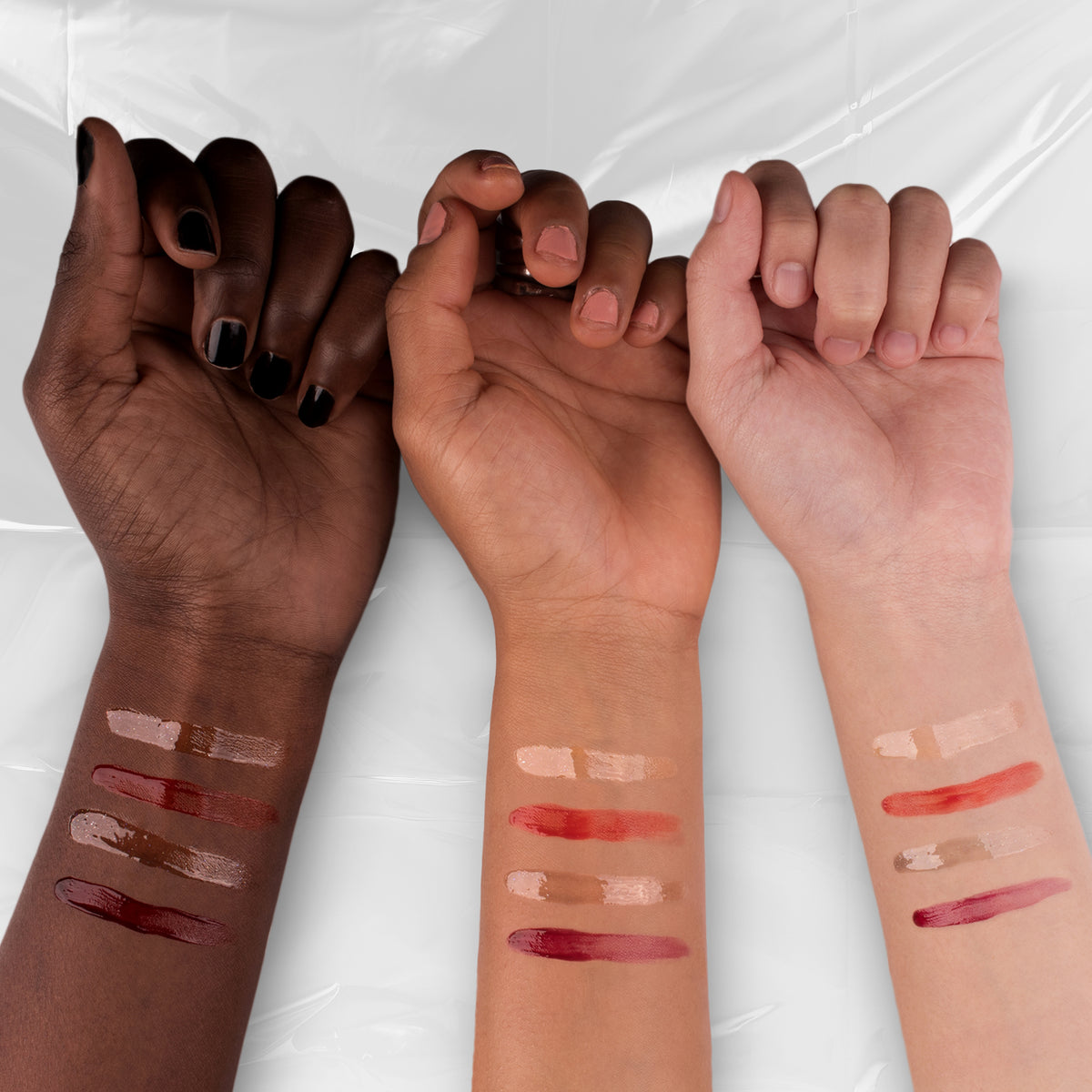 Auf der Innenseite der Unterarme von drei Armen mit unterschiedlichen Hauttönen sind Farbmuster der Lethal Cosmetics Dexter Lip Oil-Farben zu sehen.