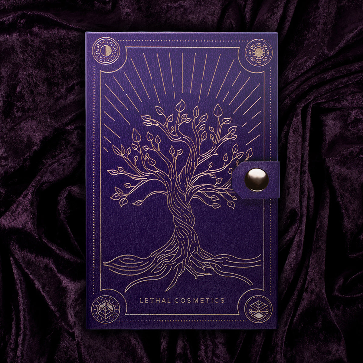 Violette Außenverpackung der Lethal Cosmetics Spellcraft Pressed Powder Palette mit goldgeprägten Baum auf einem dazu passenden violetten Samthintergrund.