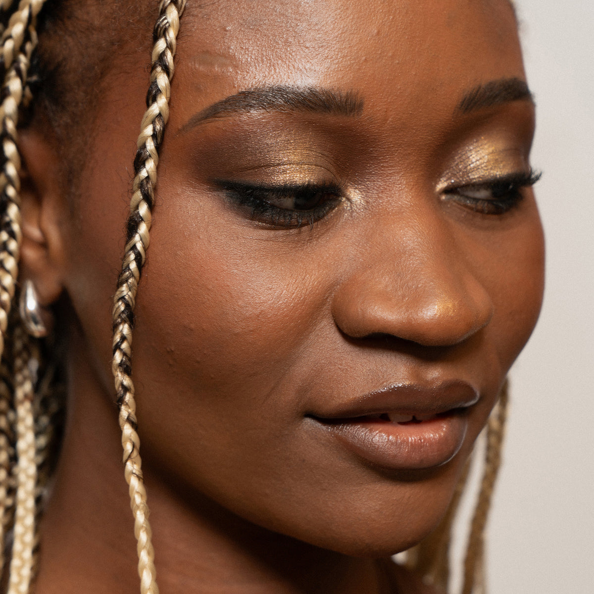 Eine Frau mit blond-braunen Braids und goldenem Augen-Make-up - mit der Boring Nude Palette von LH Cosmetics kreiert.
