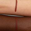 Zwei Unterarme mit je einem rötlich-braunen Lippenstift-Swatch, um die Farbwiedergabe auf heller und dunkler Haut zu zeigen.