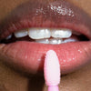 Nahaufnahme von glänzenden Lippen einer Person mit dunklem Teint und rosa Applikator des Gloil Plus von LH Cosmetics.
