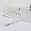 Transparenter Applikator von dem das  Gloil von LH Cosmetics auf eine weiße Oberfläche tropft; klare Tube des Produkts im Hintergrund.