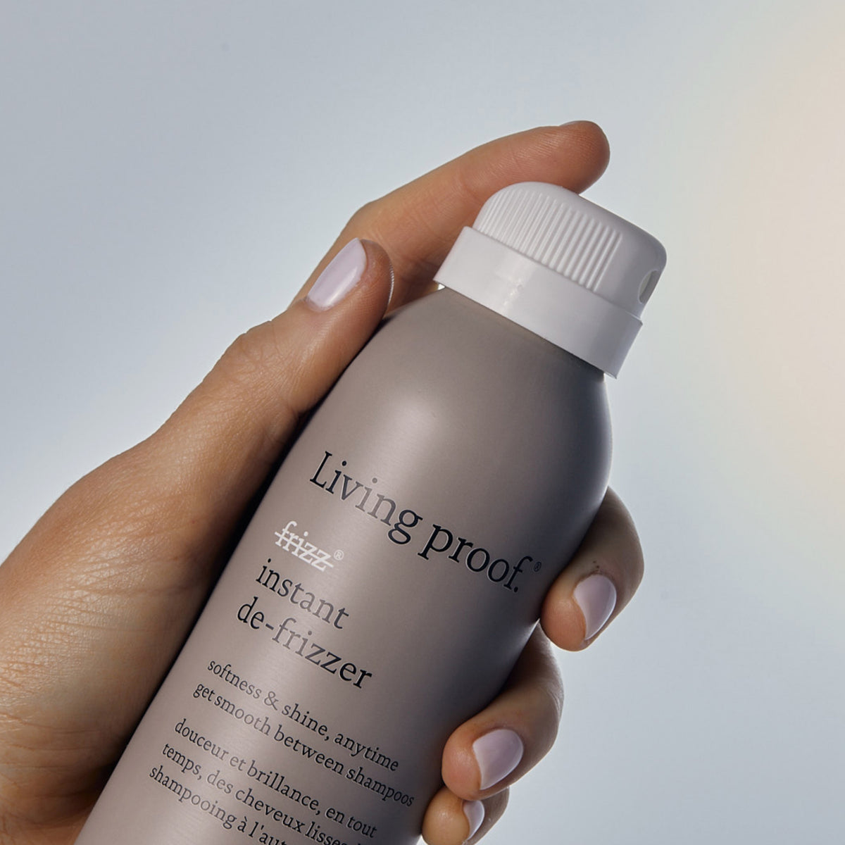 Eine Hand hält eine Dose Living Proof No Frizz Instant De-Frizzer vor einem hellen Hintergrund.