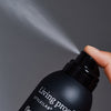 Eine Hand sprüht Living Proof Style Lab Flex Haarspray vor einem grauen Hintergrund.