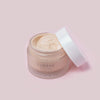 Eine geöffnete Dose Lumene INVISIBLE ILLUMINATION Instant Glow Fresh Skin Tint mit weißem Deckel ist vor einem hellrosa Hintergrund abgebildet.