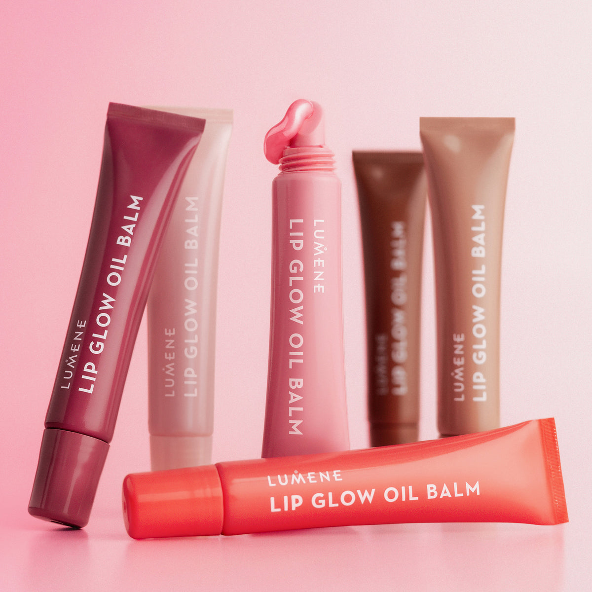 Lip Glow Oil Balm-Tuben in verschiedenen Farben vor einem rosa Hintergrund