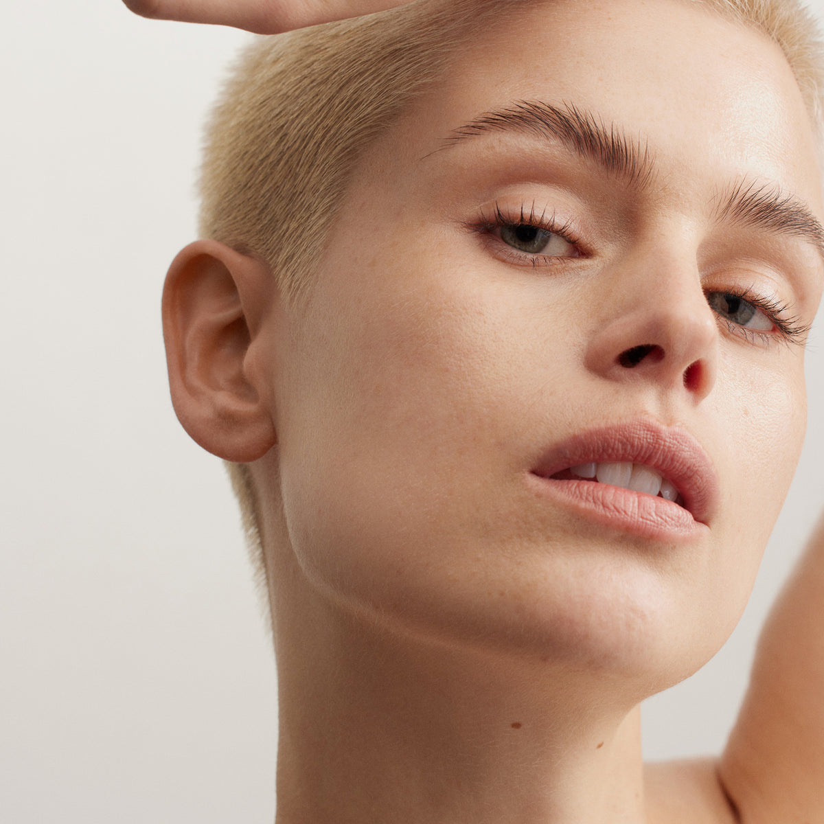 Nahaufnahme einer Person mit kurzen blonden Haaren und natürlichem Make-up, die selbstbewusst in die Kamera blickt, während sie die Lumene NORDIC SENSITIVE [HERKKÄ] Rich Day Cream präsentiert.