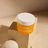 Ein oranger Tiegel Lumene NORDIC C [VALO] Day Cream SPF 30 steht auf einem beigen Block vor einem minimalistischen Hintergrund.