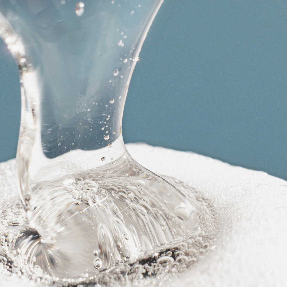 Das klare Gel von Lumene Nordic-C [VALO] Exfoliating Gel Cleanser wird auf eine weiße, schaumige Oberfläche vor einem blauen Hintergrund gegossen.