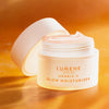 Ein geöffneter weißer Tiegel Lumene NORDIC-C [VALO] Glow Moisturizer ist auf einem orangefarbenen Hintergrund abgebildet.