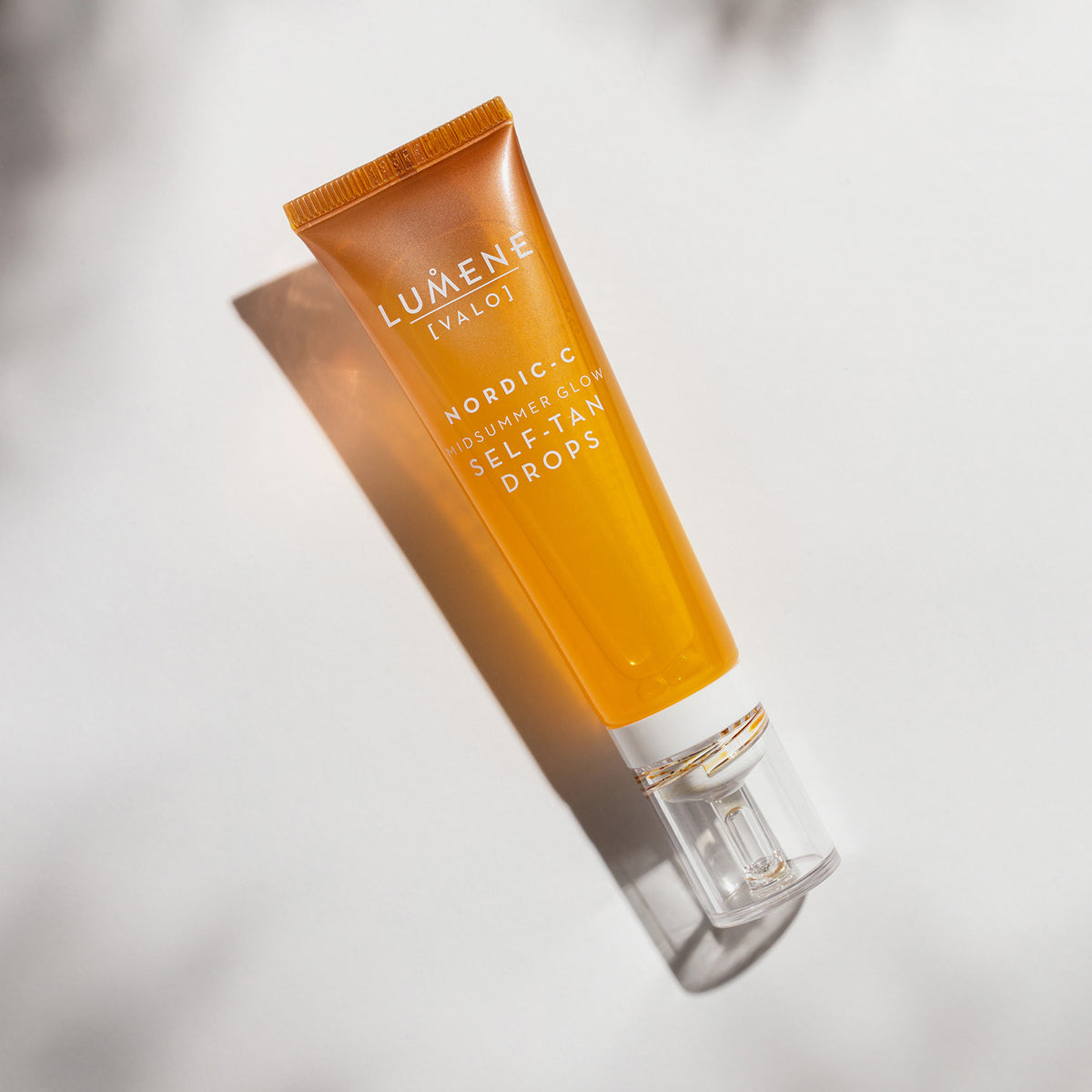 Orange-bronzene Tube Lumene NORDIC-C [VALO] Self-Tan Drops ruht auf einer hellen Fläche mit Schatten.