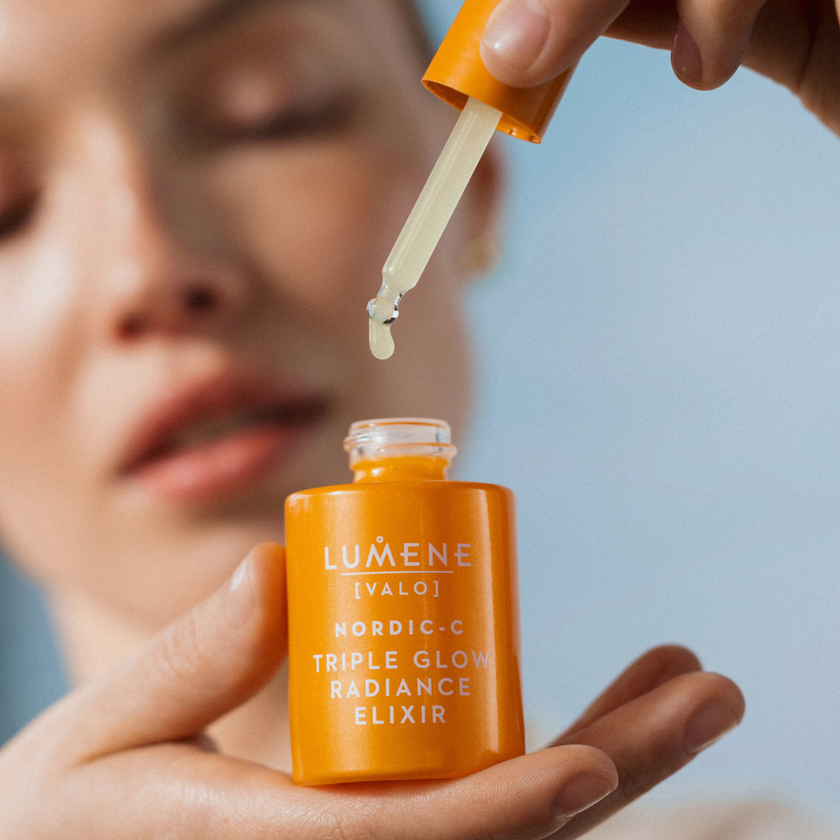 Eine Person hält einen Tropfer über eine offene Flasche Lumene NORDIC-C [VALO] Triple Glow Serum.
