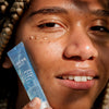Eine Person hat drei transparente Tropfen des NORDIC HYDRA [LAHDE] Purity Dew Drops Hydrating Eye Gel auf ihrer Wange  und hält die Tube daneben.