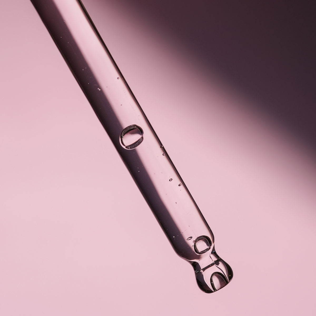 Eine Glaspipette mit klarer Flüssigkeit der Lumene NORDIC BLOOM [LUMO] Vegan Collagen Essence und Blasen vor einem rosa Hintergrund.