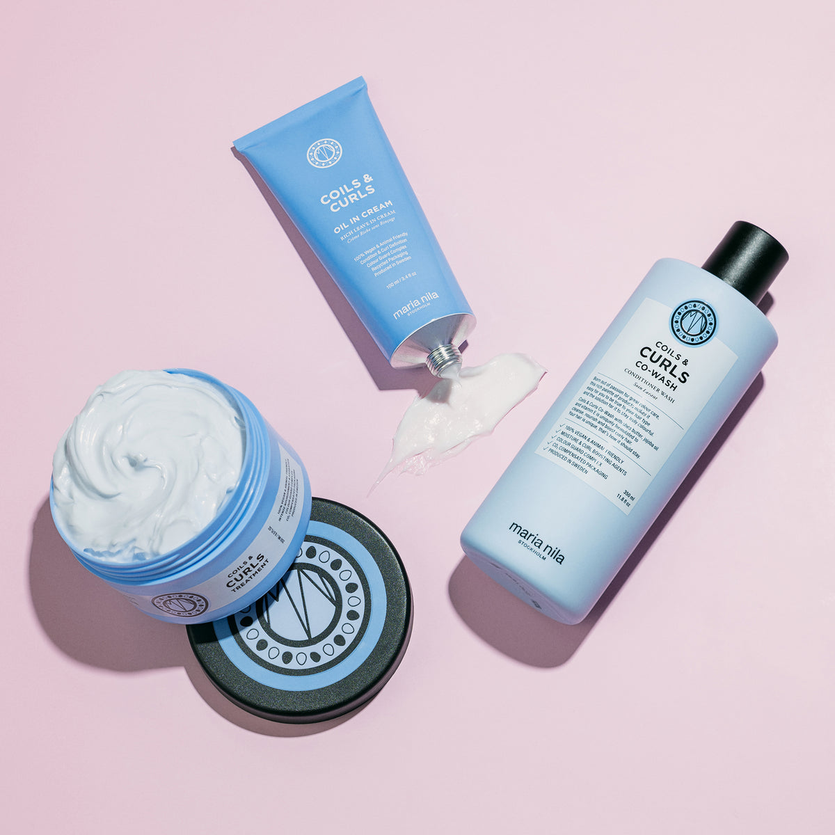 Drei blaue maria nila Coils & Curls Produkte für Locken auf rosafarbenem Hintergrund.