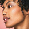 Nahaufnahme des Seitenprofils einer Frau mit klarer Haut, lockigem schwarzen Haar, das mit maria nila Coils & Curls Luscious Curl Definer gestylt wurde.