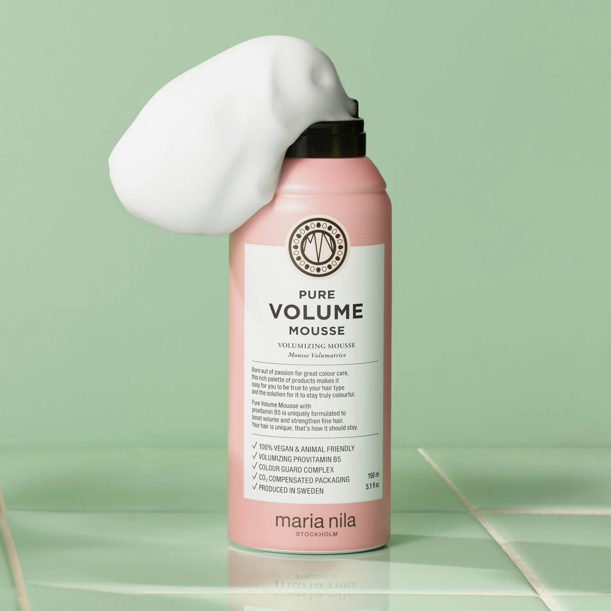 Dose maria nila Pure Volume Mousse in Rosa mit weißem Schaum auf der Spitze, vor einem grünen Hintergrund.