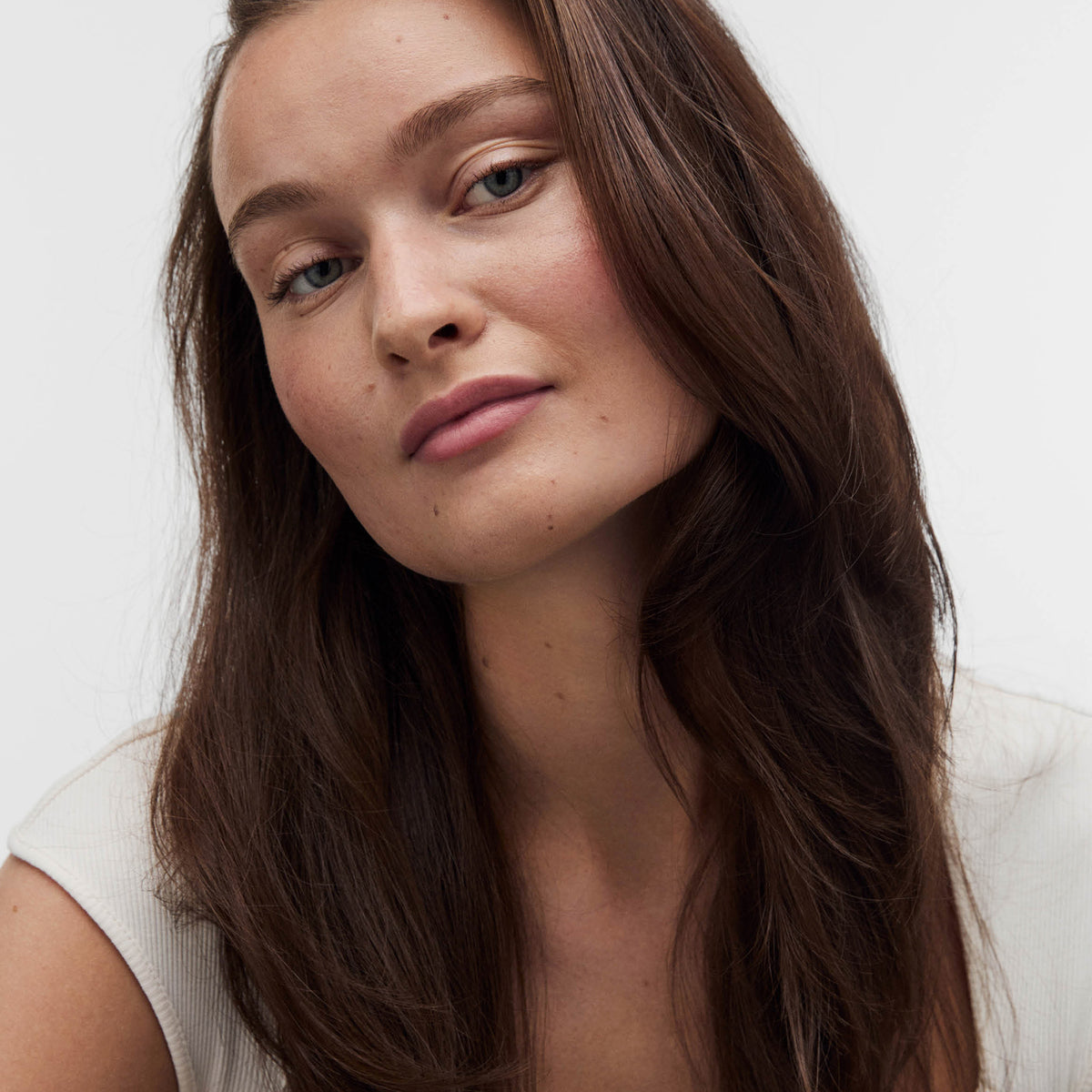 Eine Frau mit langen braunen Haaren und hellen Augen, präsentiert selbstbewusst das maria nila Pure Volume Shampoo.