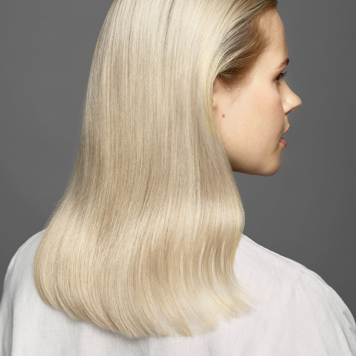 Eine Frau mit glattem, glänzendem, blondiertem Haar vor einem grauen Hintergrund nach Anwendung des maria nila Sheer Silver Conditioner.
