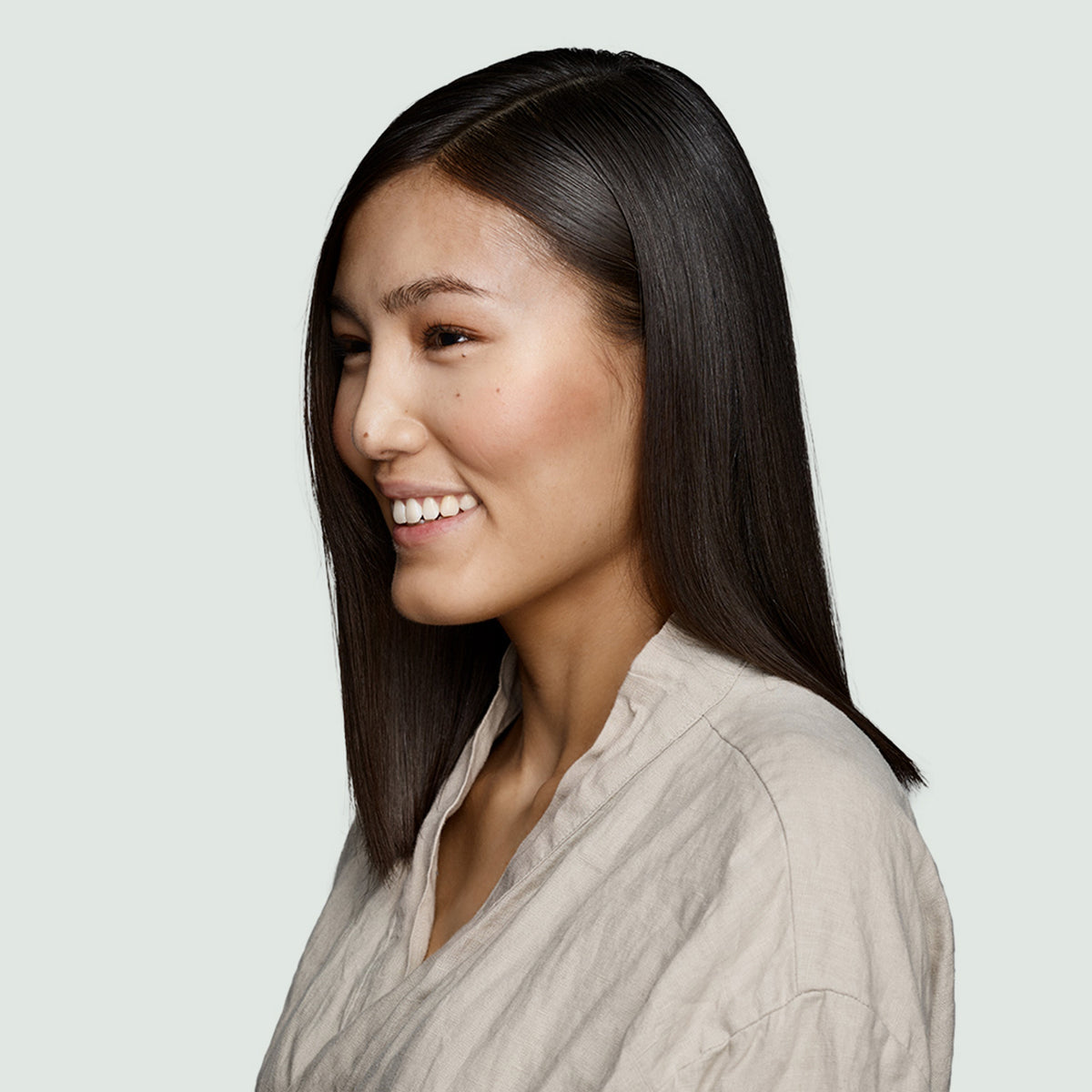 Eine Frau mit glattem dunklem Haar lächelt im Profil und wirbt für den True Soft Conditioner von Maria Nila.