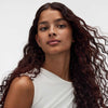 Eine Frau mit langem, lockigem Haar blickt selbstbewusst in die Kamera und präsentiert ihre gesunden Locken nach der Anwendung der True Soft Masque von Maria Nila.