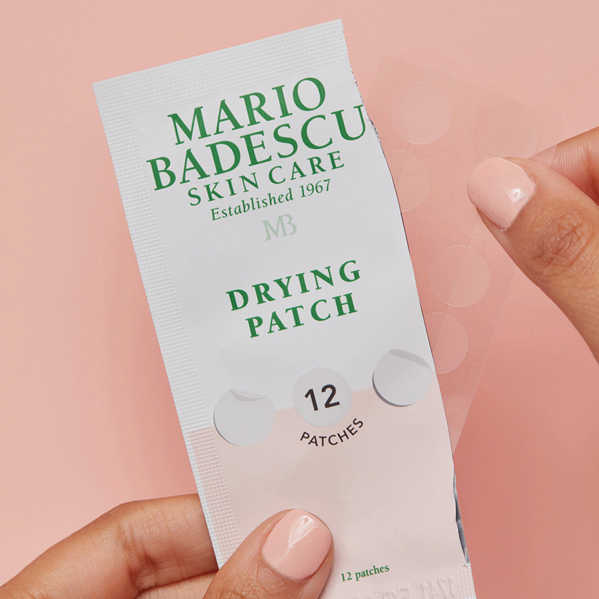 Eine Hand hält eine aufgerissene Packung Mario Badescu Drying Patch und zeigt das transparente Pflasterblatt darin.