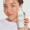 Eine lächelnde Frau hält den Mario Badescu Hydrating Glow Toner in der Hand und zeigt damit strahlende, leuchtende Haut.