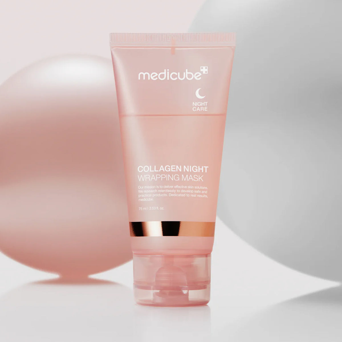 Eine rosa Tube Collagen Night Wrapping Mask steht aufrecht vor einem Hintergrund aus weichen, pastellfarbenen Kugeln.