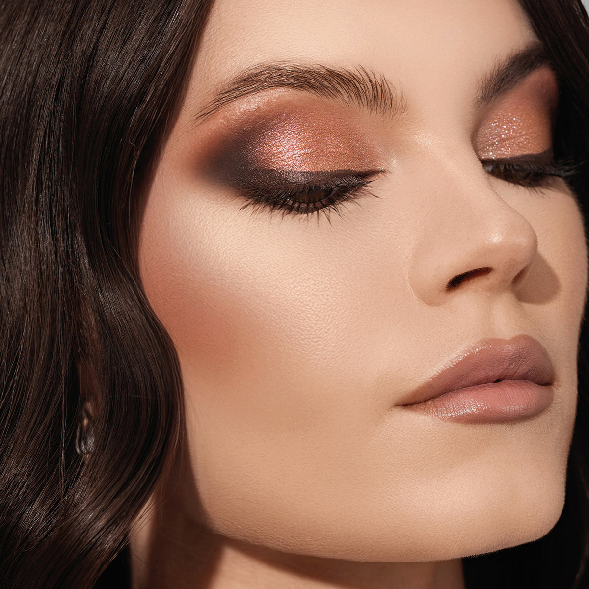 Eine Nahaufnahme einer Person mit welligem Haar, glatter Haut und schimmerndem Augen-Make-up aus der ARCHETYPE II Palette.