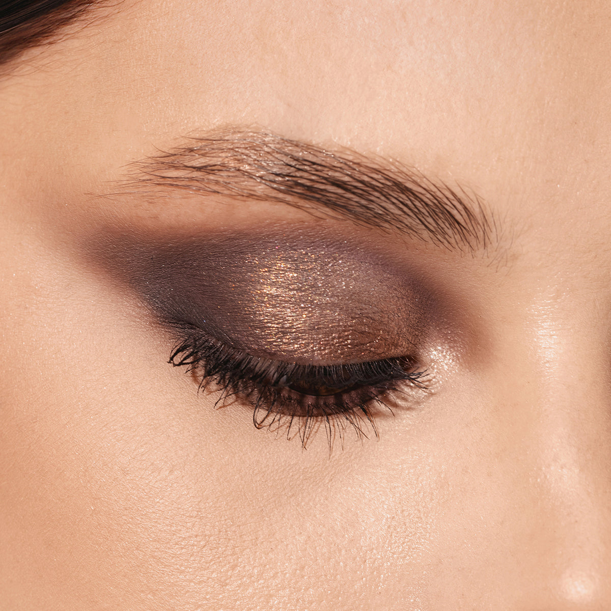 Ein geschlossenes Auge, das die ARCHETYPE-Palette von Mesauda Beauty mit einem kräftigen bronzefarbenen und dunkelbraunen Smokey-Eyeshadow zeigt.
