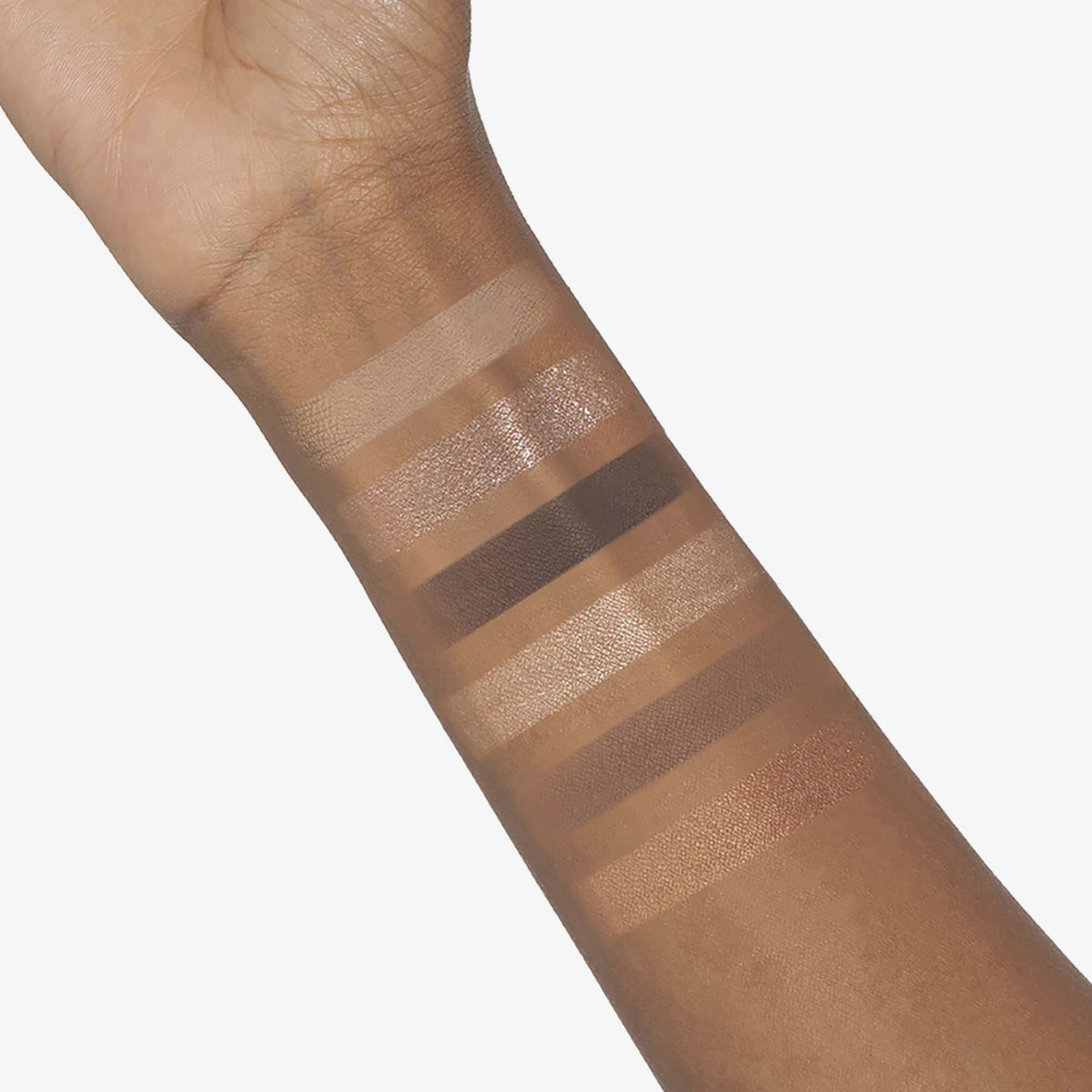 Ein Unterarm mit Swatches von sechs neutralen Farbtönen aus der Bare Harmony 2.0 Lidschattenpalette von Mesauda Beauty auf brauner Haut.