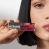 Eine Frau hält den LIPOILOGY™ Lipgloss von Mesauda Beauty in der Nähe ihres Gesichts, wobei der rosa Farbton und die silberne Kappe hervorgehoben werden.