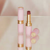Zwei Beyond Blurry-Lippenstifte in Pink und Gold, einer offen und einer geschlossen, präsentiert auf einer reflektierenden Oberfläche.