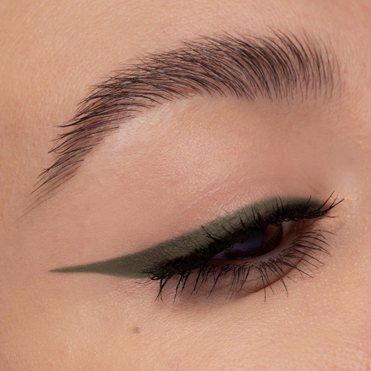Nahaufnahme eines Auges mit olivgrünem Eyeliner. Der präzise Wing zieht sich scharf nach außen, Wimpern sind betont.