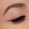 Geschminktes Auge mit rosébraunem Winged Eyeliner-Look, der sanft am äußeren Lidrand ausläuft. Die Wimpern sind schwarz und definiert.