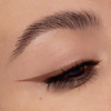 Nahaufnahme eines geschminkten Auges mit braunem Lidschatten und präzisem, mattem braunen Eyeliner-Wing. Wimpern sind leicht getuscht.