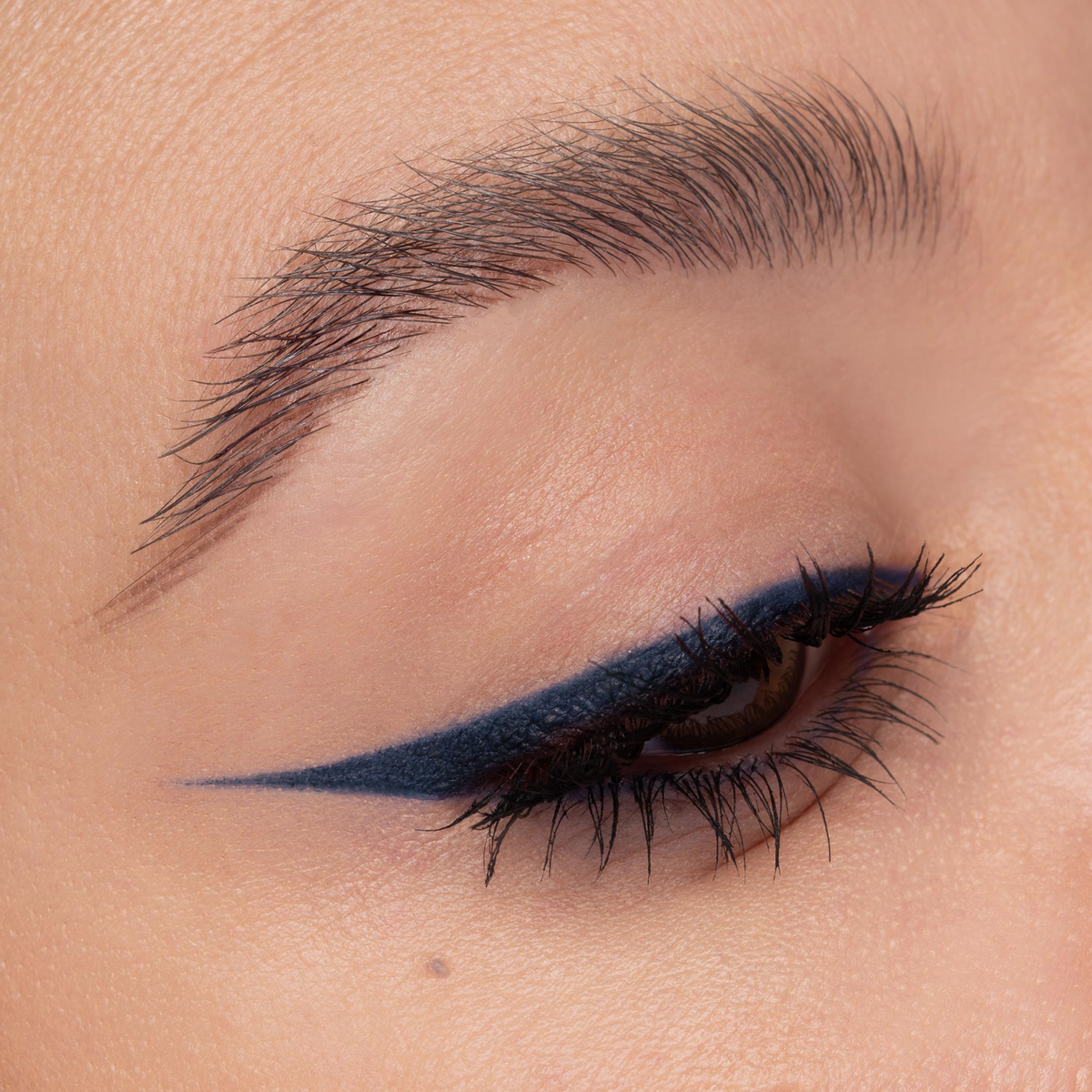 Nahaufnahme eines Auges mit blauem Eyeliner. Der präzise Wing zieht sich scharf nach außen, Wimpern sind betont.