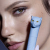 Eine Frau hält Vicious Mascara Waterproof mit einer katzenförmigen Kappe vor ihr Gesicht und betont so ihre langen Wimpern.