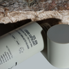 Eine Flasche NERDS. 12% AHA Liquid Exfoliant liegt mit abgenommenem Deckel auf der Seite und ruht unter einem strukturierten Stein.