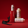 Drei Flaschen mit Haarpflegeprodukten aus dem OLAPLEX Total Hair Repair Holiday Kit 2026, die auf und neben einer mit einem schwarzen Band verzierten Geschenkbox angeordnet sind.