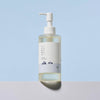 Mattiert transparente Flasche des 1025 Dokdo Cleansing Oil von Round Lab mit Pumpspender auf hellem Untergrund vor blauem Hintergrund.