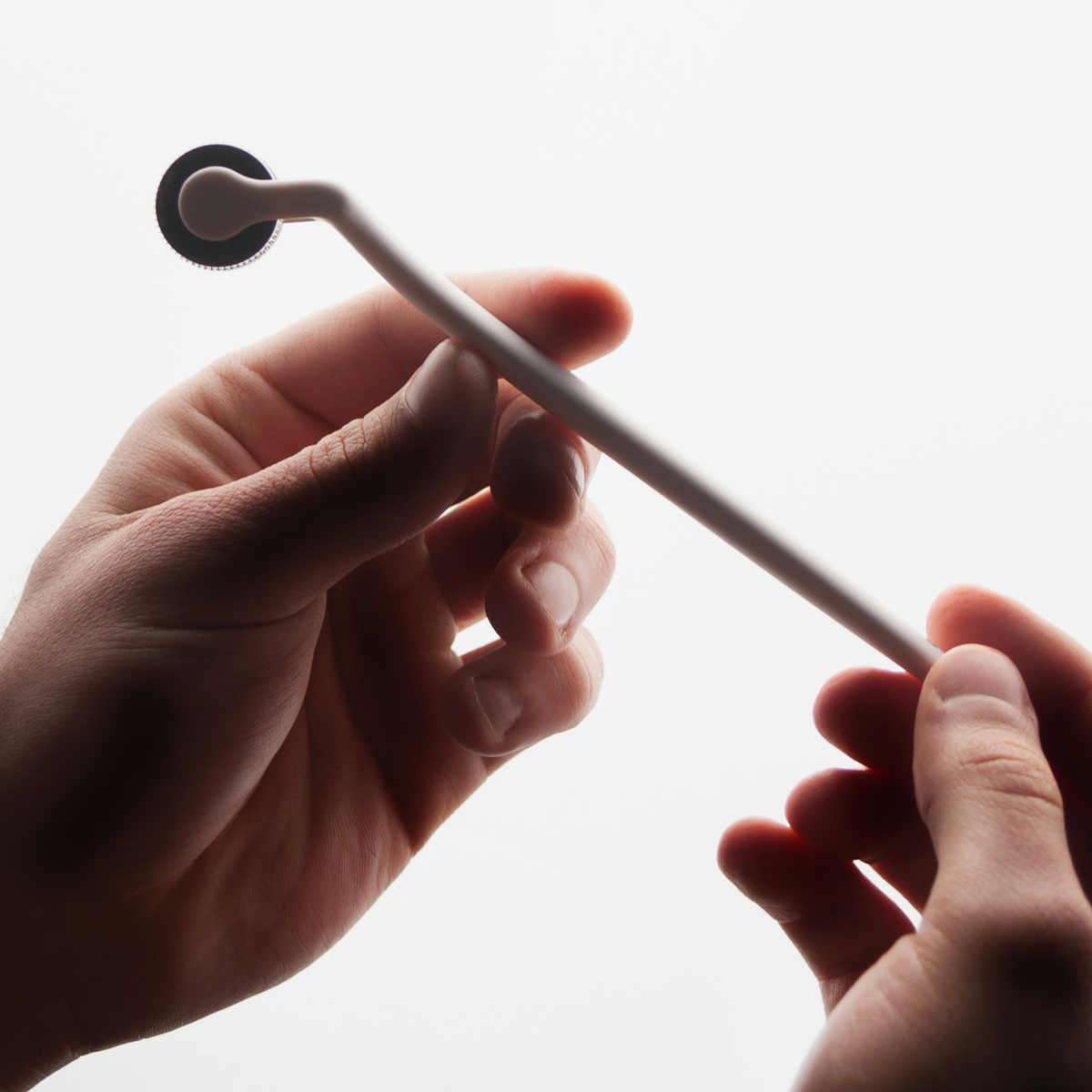 Eine Person hält den Scandinavian Biolabs Scalp Activation Derma Roller mit langem weißen Griff und einem kleinen Stachelrad vor einem weißen Hintergrund.