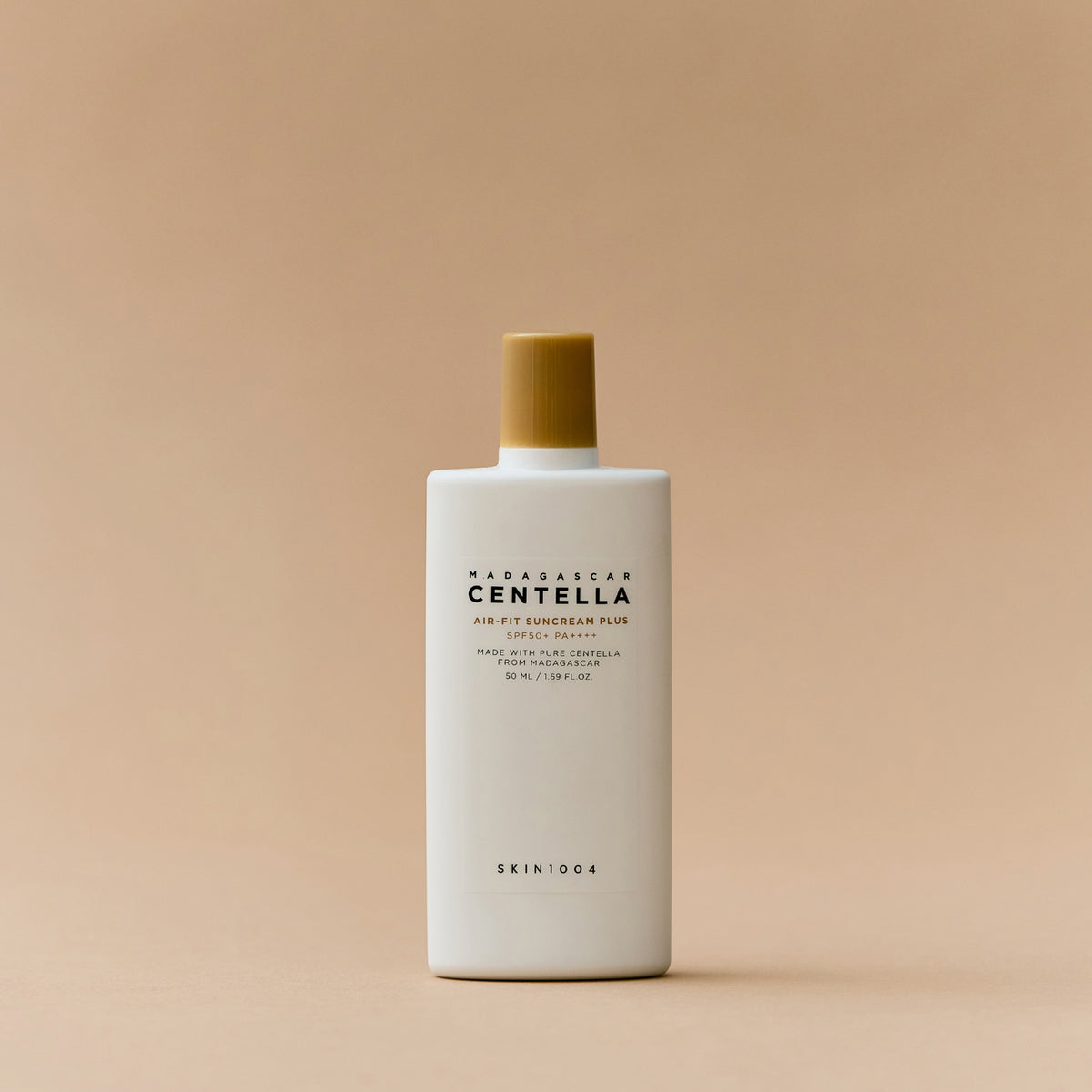 Eine weiße Flasche Madagascar Centella Air-Fit Suncream Plus mit goldenem Deckel auf beigem Hintergrund.