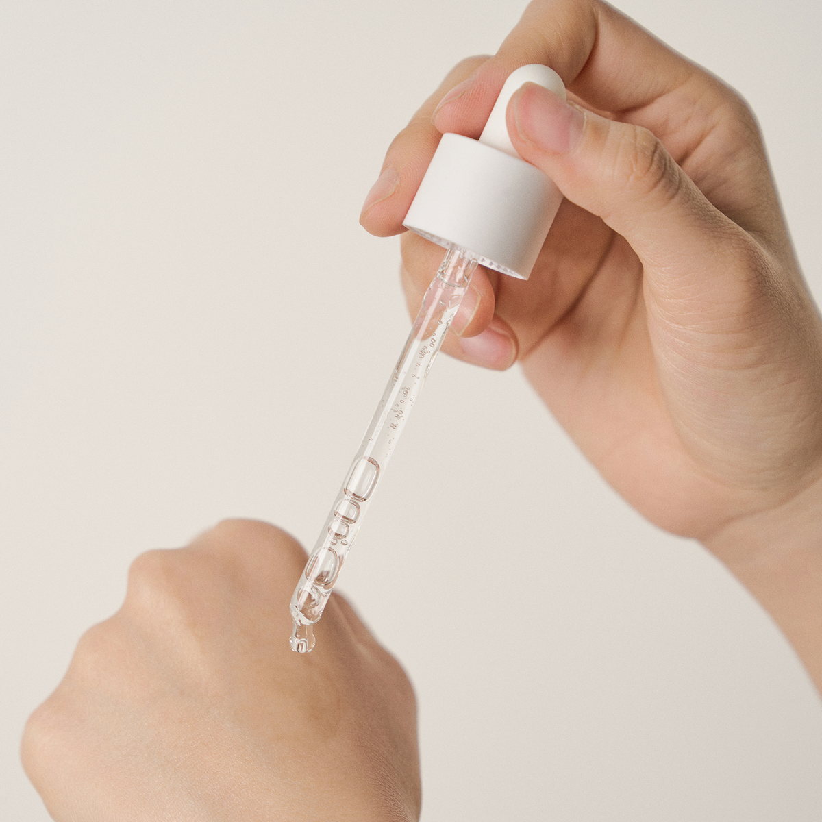 Eine Hand trägt mit einer Pipette die klare Flüssigkeit Madagascar Centella Poremizing Fresh Ampoule von SKIN1004 auf den Rücken einer der Hand auf.