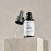 Eine Flasche Lunar Serum Concentrate mit einer Pipette steht vor einem neutralen Hintergrund auf einem Betonblock.