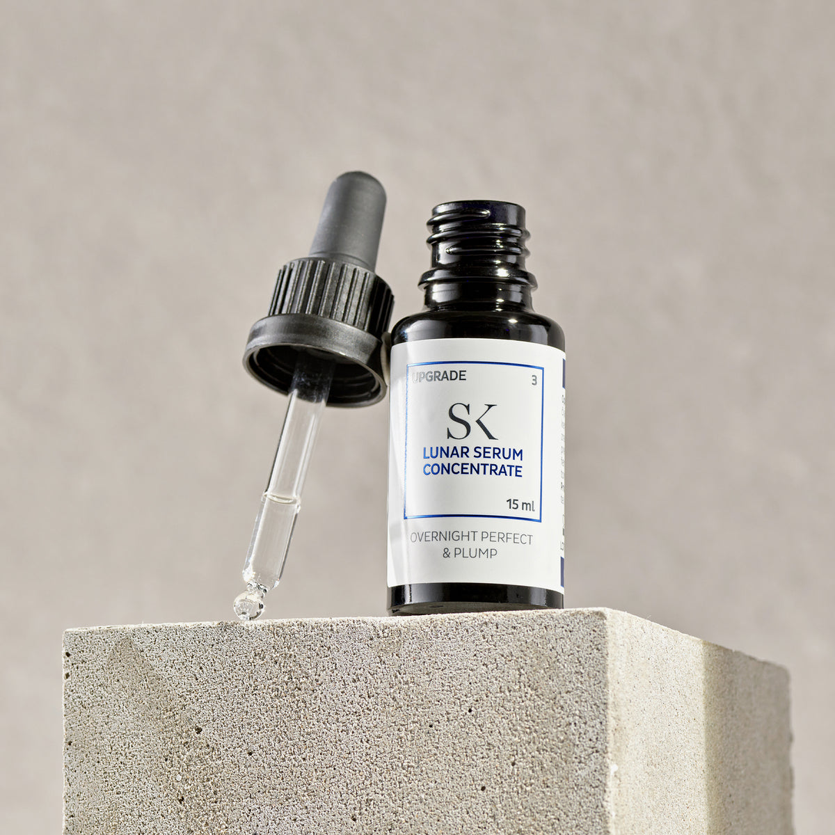 Eine Flasche Lunar Serum Concentrate mit einer Pipette steht vor einem neutralen Hintergrund auf einem Betonblock.