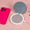 Eine rosa Handyhülle und ein Flip n Charge Power Bank Compact LED Mirror mit Kabeln auf einer rosa Oberfläche.