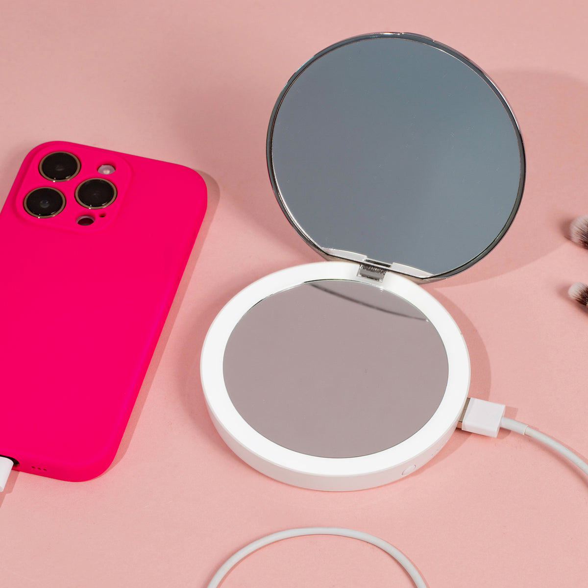 Eine rosa Handyhülle und ein Flip n Charge Power Bank Compact LED Mirror mit Kabeln auf einer rosa Oberfläche.