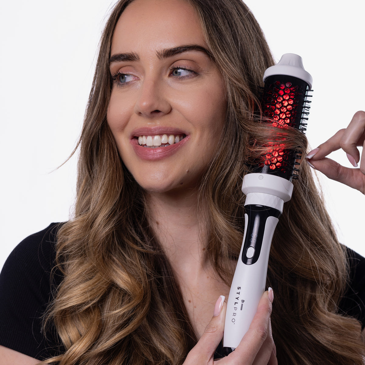 Eine lächelnde Frau stylt ihr Haar mit der STYLPRO Near-Infrared Heated Hairbrush, die mit einem roten Licht leuchtet.