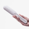 Eine Hand hält die STYLPRO Re-Growth Red Light Hair Brush, ein weißes elektronisches Gerät mit Tasten und Kontrollleuchten.